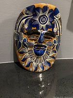 Frontal view of the handmade Mexican terracotta face mask showing detailed floral and swirl paint in blue, white, and gold.