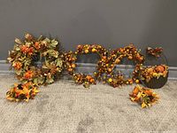 Full view of all fall-themed artificial wreaths and decorative pieces arranged on carpet against grey wall, highlighting size and number of items