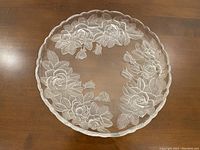 Top view of the round glass serving platter showing detailed frosted floral rose and leaf pattern surface and scalloped edges.