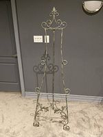 Full view of the metal art display easel standing against a gray wall, showing its full height and structure.