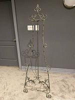 Front view of metal art display easel showing decorative curls, scrollwork, and antique finish.