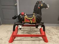 Front-side view of black plastic rocking horse on a red metal spring frame showing painted gold and red saddle details and white horse markings