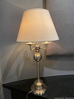 Angle view of the table lamp showing the silver metal base and white fabric shade