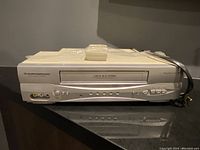 Front view of Durabrand VHS video cassette recorder showing front panel with cassette slot, AV ports, control buttons, and remote on top.