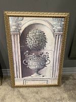 Front view of wall art depicting classical urn and topiary, framed in ornate gold frame.