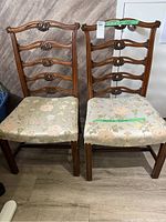 Front view of two wooden chairs side by side showing floral seat upholstery and carved wooden backs.