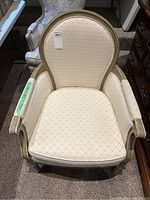 Full front view of the cream upholstered vintage accent chair showing padded seat, tufted back, and carved wooden frame with distressed paint.