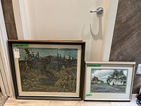 Full view of two framed artworks leaning against a wall, showing relative sizes and framing styles.