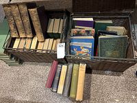 Two wire baskets each holding multiple hardcover books in leather and cloth bindings, front row of seven books removed for identification