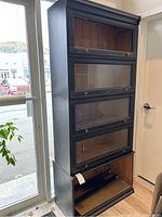 Full view of assembled four-section bookcase, showing black exterior and glass-front doors.