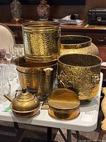 Wide shot showing all brass pots and accessories on a table including teapot, candlestick holder, and lidded container