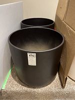Two large black ceramic pots standing next to cardboard box and wall corner, showing exterior condition and size.