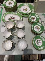 Full spread showing stacks of plates, cups, saucers and three serving dishes in green pheasant pattern