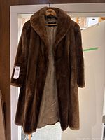 Full front view of the vintage brown fur coat hanging, showing the wide collar and interior lining.