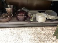 Shelf with various cooking and baking dishes including glass pot, white baking dishes, platters, and metal bowls.