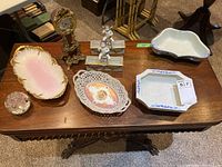 Table display of seven decorative items including ceramic serving dishes, porcelain plate, ornate clock, glass paperweight and cherub trinket holders