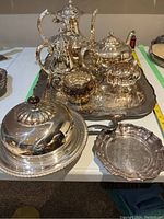 Overview of entire set showing five-piece EP silver tea set arranged on a large engraved rectangular silver-plated tray, Birks muffin warmer dish with lid in foreground, and small Birks Regency plate to the right.