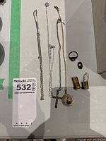 Overview of three chains with pendants, ring, pin, and small religious figure in gold-tone vessel captured on white surface.