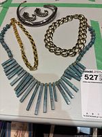 Top view showing full assortment of five necklaces and two brooches on white surface with green taped border.