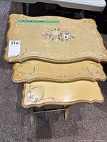Three wooden nesting tables stacked showing hand painted flower patterns and scalloped edges on tops.