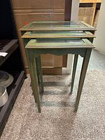 Set of three green nesting tables with distressed gold trim and glass tops, nested together