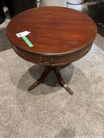 Photo of full round wooden table with curved legs and some visible surface wear.