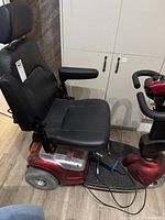 Left side view showing red base, black vinyl seat, armrest and charger cable on foot platform