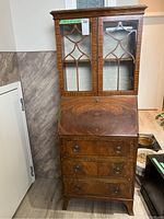 Full view of vintage wooden secretary desk with glass doors and drawers, showing overall condition.