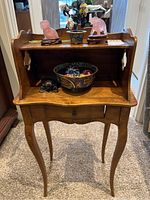 Front view of wooden small table with drawer, topped with various decorative items including carved pink stone animal figurines, turtle figurine, ceramic pot, and bowl.