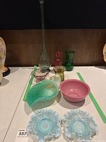 Tabletop display showing pair of pale blue hobnail candy dishes, green and white swirl leaf dish, pink opaque bowl, lavender footed bowl, square-based olive green vase, pale green slender-neck flask vase, red ribbed bud vase, and green footed bud vase