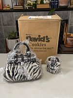 Two zebra print handbag-shaped porcelain cookie jars with black handles, one large and one miniature, wrapped in plastic with a David's Cookies cardboard box in the background.