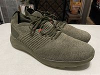 Side-top angle of right sneaker showing knit texture upper, olive green color and lace-up closure.
