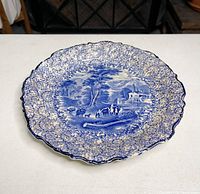 Blue transferware plate by J. Kent Fenton with scenery and floral edge detail, displayed flat on table.