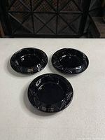Three vintage black glass ashtrays on white surface showing gold embossed Reno, The Fun, and Nevada text and fluted edges.