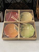 Four heirloom tomato shaped side dish bowls, each a different color, packaged in original box tied with raffia ribbon