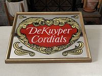 Front view of the DeKuyper Cordials mirror sign showing the red heart logo and ornate gold decorations on a mirror background within a gold frame.