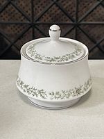 Front view of closed Mikasa sugar bowl showing detailed green vine decoration with silver trim on lid and body.