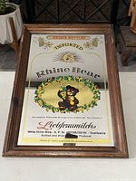 Full view of the vintage Rhine Bear imported mirror sign with bear holding grapes graphic and wood frame on the floor.