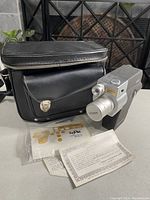 Vintage Vernon Zoom movie camera shown with side and front view, including lens and name plate, on table with black carrying case and instruction papers.