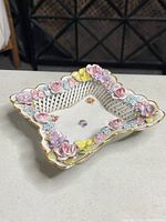 Top angle view of square lattice porcelain bowl with open weave sides and multi-colored 3D flowers with gold trimmed scalloped edges.