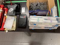 Overview of all lot items on table including storage boxes, tweezers, caulking tips, pouches, pill organizer, fire extinguishers and playing cards.