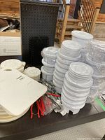Multiple stacks of white rotating plastic paint palette trays with eight wells and central reservoir; small white flower-shaped palettes; red-handled pliers; white rectangular boards; black pegboard display panel