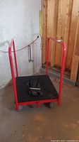 Front view of red platform cart showing black deck, tubular handles, caster wheels and included strap