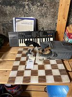 Marble chess board with brown and white marble squares on a wooden shelf, with marble chess pieces and Realistic Concertmate-500 electronic keyboard with accompanying manual and cables.
