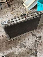 Folded foldable ramp showing carry handle and rubber feet on rough floor with dirt and debris.