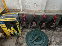 Four black MotoMaster 2 ton jack stands arranged side by side and two yellow Powerfist 3 ton jack stands in original box.