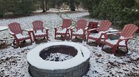 Six red plastic Muskoka chairs arranged around a stone fire pit outdoors with snow on ground and chairs.