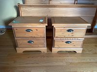 Pair of matching wooden night tables with two drawers, showing front view with metal cup handles and some scratches on surface and edges.