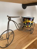 Glass planter pot in decorative metal bicycle stand on wooden shelf, showing entire sculpture from side angle.