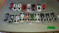 Top down photo showing 18 assorted diecast race cars arranged in plastic trays on table.